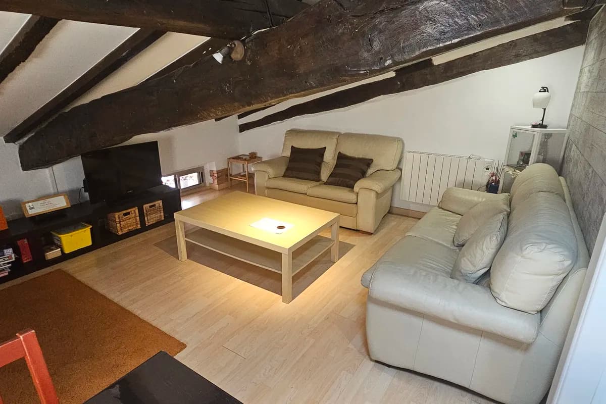 Zona de estar con sofás, televisión y vigas de madera
